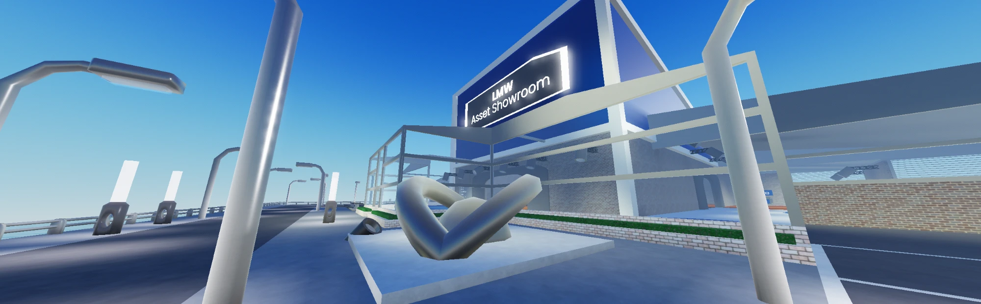 A chrome sculpture on a plinth in the forecourt, with the glowing sign and glazed entrance behind it.